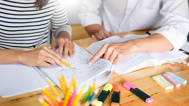 Zwei Menschen sitzen an einem Tisch und arbeiten in einem Heft.