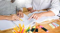 Zwei Menschen sitzen an einem Tisch und arbeiten in einem Heft.