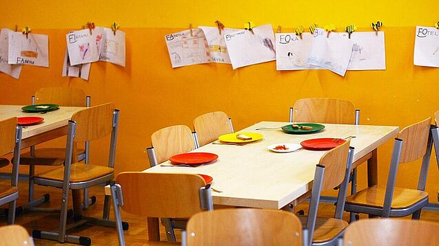 Tische in einer Schule sind gedeckt mit Tellern und Besteck.