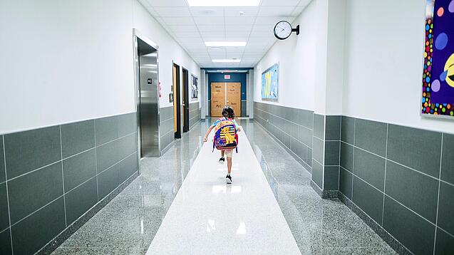 Kleines Kind mit Rucksack läuft über einen Schulflur.