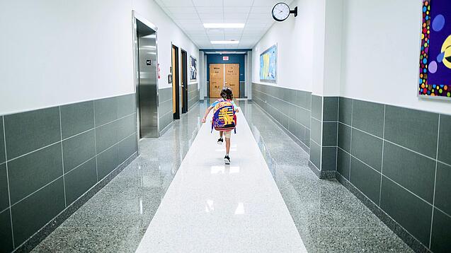 Kleines Kind mit Rucksack läuft über einen Schulflur.