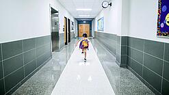 Kleines Kind mit Rucksack läuft über einen Schulflur.