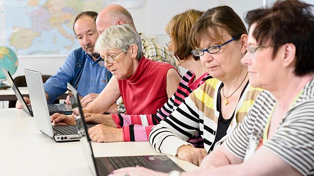 Eine Gruppe Senior:innen sitzt vor Laptops.