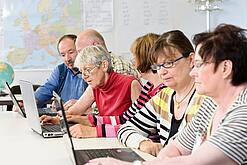 Eine Gruppe Senior:innen sitzt vor Laptops.