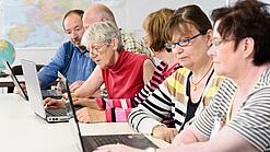 Eine Gruppe Senior:innen sitzt vor Laptops.