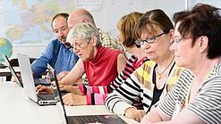 Eine Gruppe Senior:innen sitzt vor Laptops.