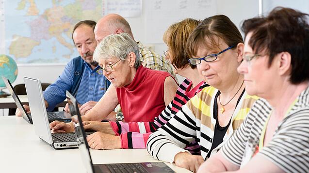Eine Gruppe Senior:innen sitzt vor Laptops.