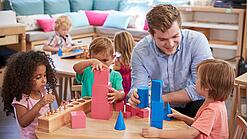 Ein Erzieher mit drei Kindern an einem Tisch, sie spielen mit Bauklötzen.