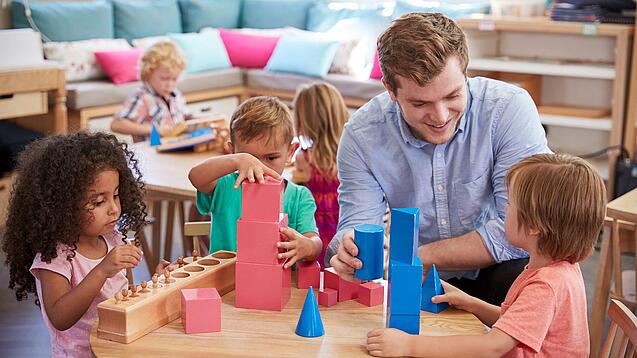 Ein Erzieher mit drei Kindern an einem Tisch, sie spielen mit Bauklötzen.