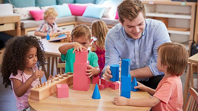 Ein Erzieher mit drei Kindern an einem Tisch, sie spielen mit Bauklötzen.