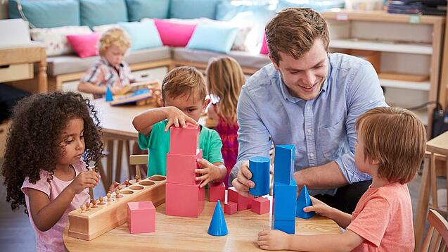 Ein Erzieher mit drei Kindern an einem Tisch, sie spielen mit Bauklötzen.