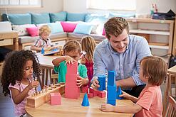 Ein Erzieher mit drei Kindern an einem Tisch, sie spielen mit Bauklötzen.