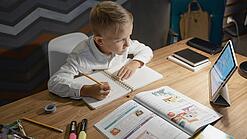 Junge sitzt an einem Schreibtisch und macht Schularbeiten mit einem Tablet.