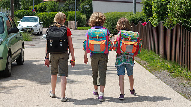 Drei Grundschulkinder mit Schulranzen auf dem Rücken.