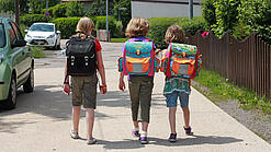 Drei Grundschulkinder mit Schulranzen auf dem Rücken.
