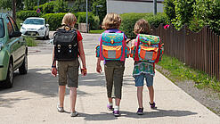 Drei Grundschulkinder mit Schulranzen auf dem Rücken.