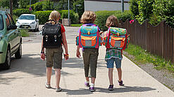 Drei Grundschulkinder mit Schulranzen auf dem Rücken.