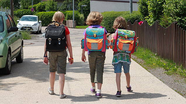 Drei Grundschulkinder mit Schulranzen auf dem Rücken.