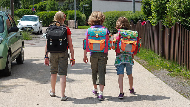 Drei Grundschulkinder mit Schulranzen auf dem Rücken.