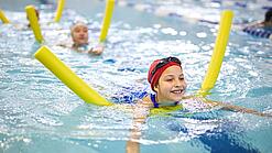 Kinder schwimmen mit Poolnudel in einem Schwimmbecken.