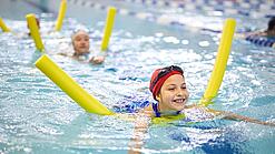 Kinder schwimmen mit Poolnudel in einem Schwimmbecken.
