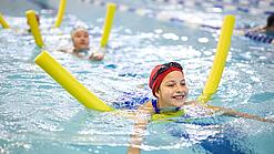 Kinder schwimmen mit Poolnudel in einem Schwimmbecken.
