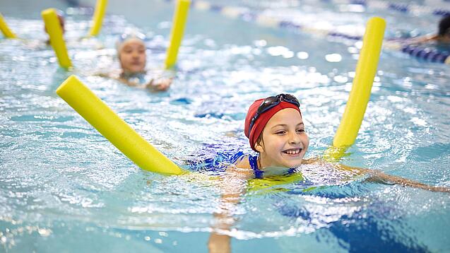 Kinder schwimmen mit Poolnudel in einem Schwimmbecken.