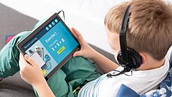 Ein Kind mit Kopfhörern lernt mit einem Tablet auf dem Schoß für Mathematik.