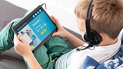 Ein Kind mit Kopfhörern lernt mit einem Tablet auf dem Schoß für Mathematik.