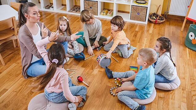 Erzieherin und eine Gruppe Kinder musizieren.