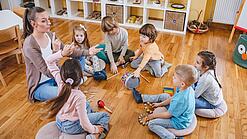 Erzieherin und eine Gruppe Kinder musizieren.