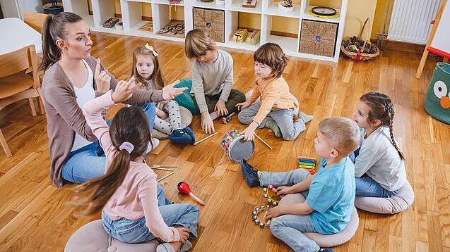 Erzieherin und eine Gruppe Kinder musizieren.