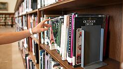 Eine Hand greift nach einem Buch in einem großen Bücherregal.