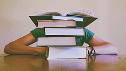 Ein Mensch sitzt hinter einem Stapel Bücher und ist dadurch nicht weiter erkennbar.