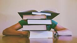 Ein Mensch sitzt hinter einem Stapel Bücher und ist dadurch nicht weiter erkennbar.