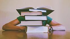 Ein Mensch sitzt hinter einem Stapel Bücher und ist dadurch nicht weiter erkennbar.