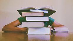 Ein Mensch sitzt hinter einem Stapel Bücher und ist dadurch nicht weiter erkennbar.