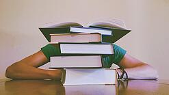 Ein Mensch sitzt hinter einem Stapel Bücher und ist dadurch nicht weiter erkennbar.