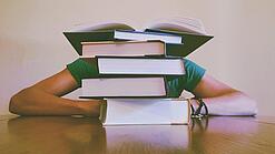 Ein Mensch sitzt hinter einem Stapel Bücher und ist dadurch nicht weiter erkennbar.