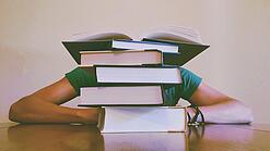 Ein Mensch sitzt hinter einem Stapel Bücher und ist dadurch nicht weiter erkennbar.