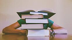 Ein Mensch sitzt hinter einem Stapel Bücher und ist dadurch nicht weiter erkennbar.