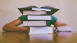 Ein Mensch sitzt hinter einem Stapel Bücher und ist dadurch nicht weiter erkennbar.
