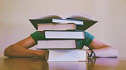 Ein Mensch sitzt hinter einem Stapel Bücher und ist dadurch nicht weiter erkennbar.
