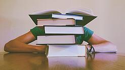 Ein Mensch sitzt hinter einem Stapel Bücher und ist dadurch nicht weiter erkennbar.