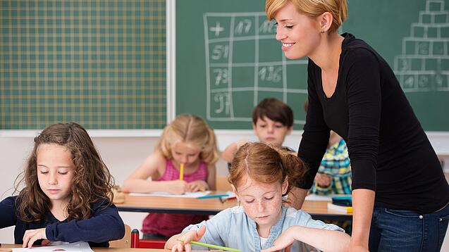 Junge Lehrerin beaufsichtigt Kinder in einer Grundschulklasse.