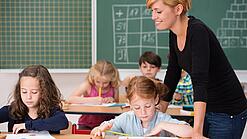 Junge Lehrerin beaufsichtigt Kinder in einer Grundschulklasse.