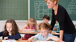 Junge Lehrerin beaufsichtigt Kinder in einer Grundschulklasse.