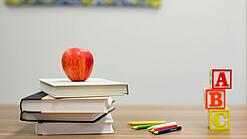 Mehrere Bücher, ein Apfel, Stifte und Bauklötze liegen auf einem Tisch.