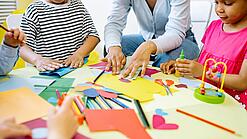 Kindergartenkinder und eine Betreuerin basteln an einem Tisch.