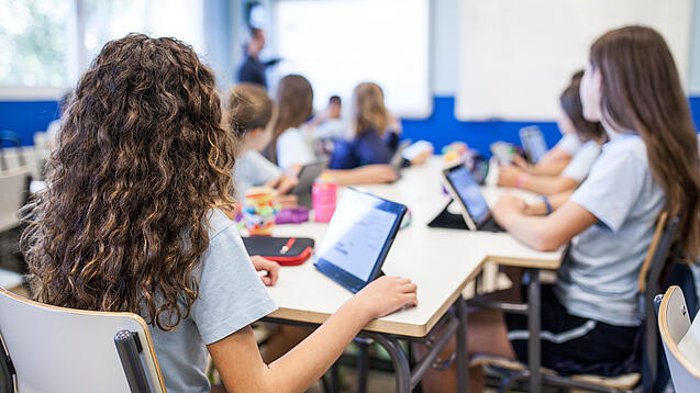 Schülerinnen sitzen in einem Klassenraum an einem Tablet.